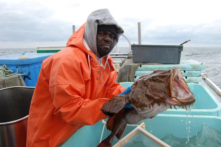 Larry Alade holding a goosefish with it's mouth open over blue bins.