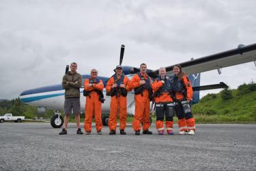 Photo of team standing in orange flight suits on the tarmac in front of NOAA Twin Otter aircraft.