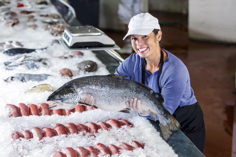 Woman holding fish at seafood counter. 