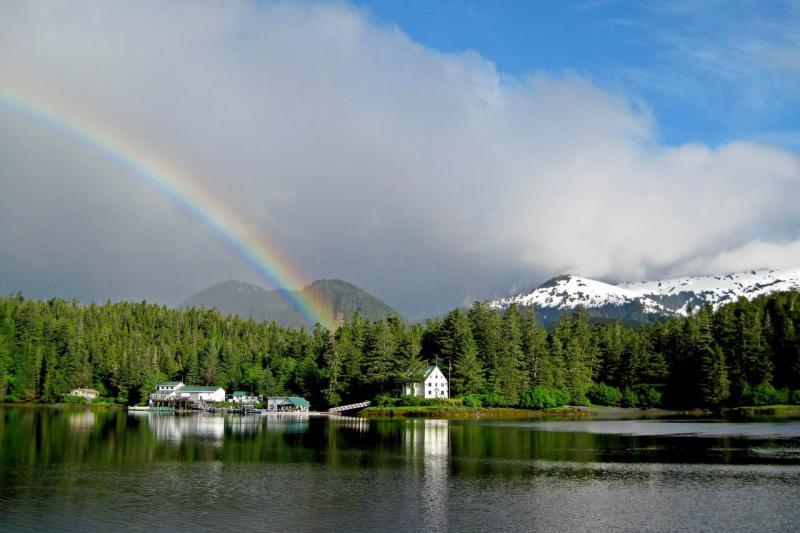 Photo of the Little Port Walter Marine Research Station, with a rainbow and mountains in the background, viewed from the water.