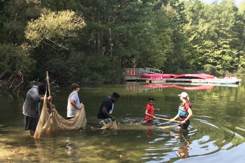 Four students and a teacher wade into a creed with a large fish net