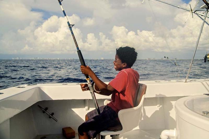 A smiling child reels in his catch while seated on a fishing boat.