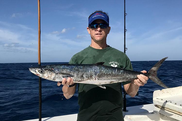Recreational fisherman holding up long, narrow, gray, and silver king mackerel fish.