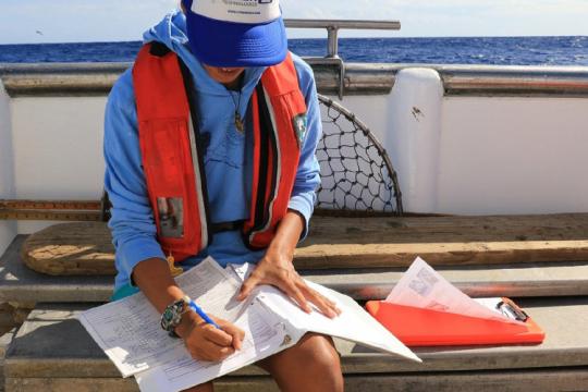 Fisheries observer taking notes on a boat deck.