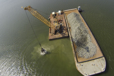 A crane moves material to build an oyster reef from a barge into the Piankatank River.
