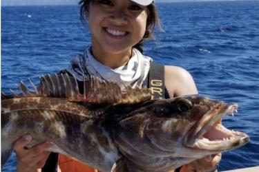 Young female scientist on a survey vessel smiling and holding a large groundfish