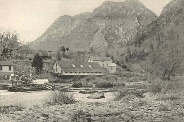 Wooden buildings of Baird Station, with McCloud River in the foreground, mountains behind