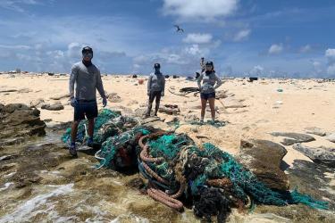 Three people stand around a large net that has washed up on a remote beach