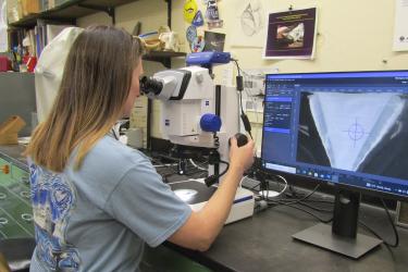 Scientist looking through a microscope. A magnified shark vertebra is displayed on a computer screen. 