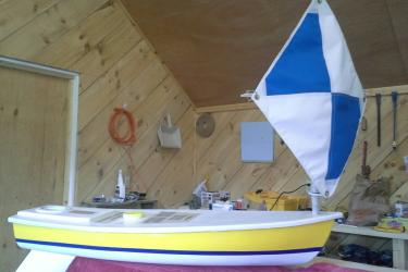 Yellow miniboat with blue and white sail on workbench.