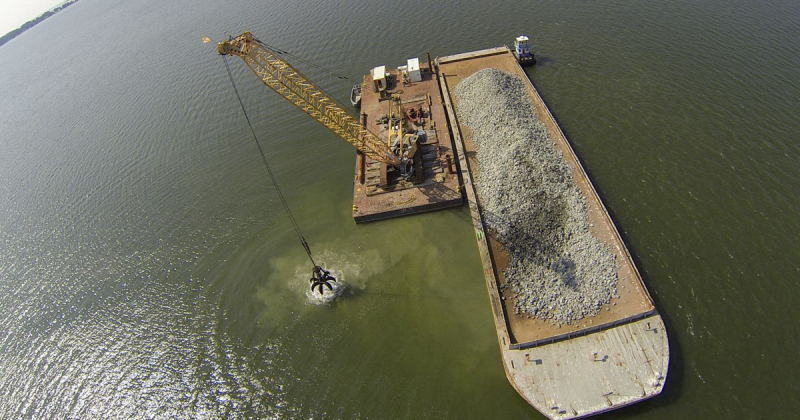 A crane moves material to build an oyster reef from a barge into the Piankatank River.