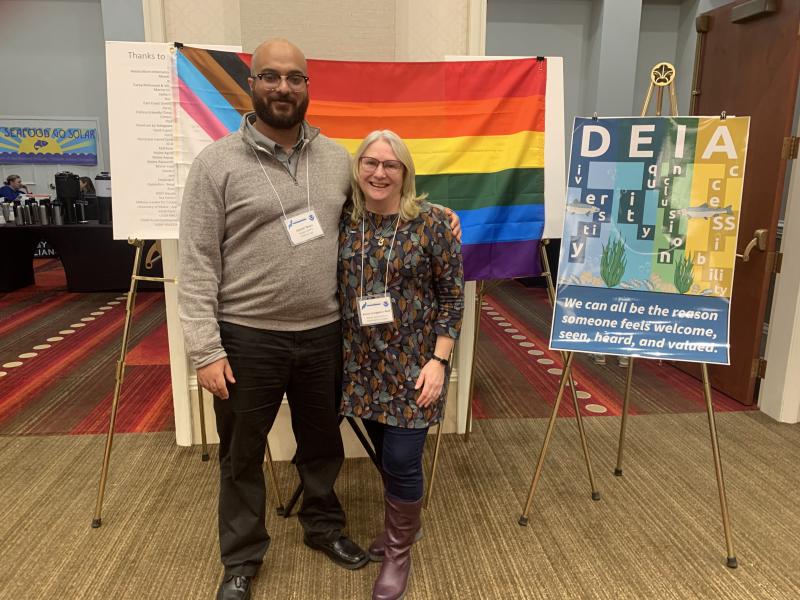 A man (left) and woman (right) stand in front of a pride flag and a poster with the words “diversity, equity, inclusion, and accessibility”.  Credit: NOAA Fisheries/Lisa Milke